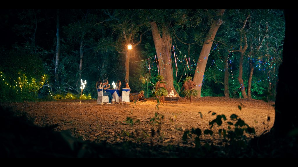 A magical forest-themed dinner setup with tribal dance performance at the best resorts in Dandeli, featuring guests dining under fairy lights and enjoying a bonfire amidst nature.
