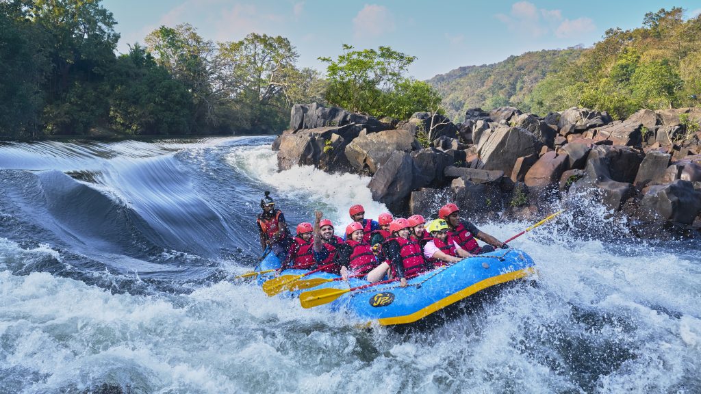 Group of adventurers enjoying white-water rafting near the best resorts in Dandeli, surrounded by rocky rapids and lush forest landscapes | Whsitling Woodzs